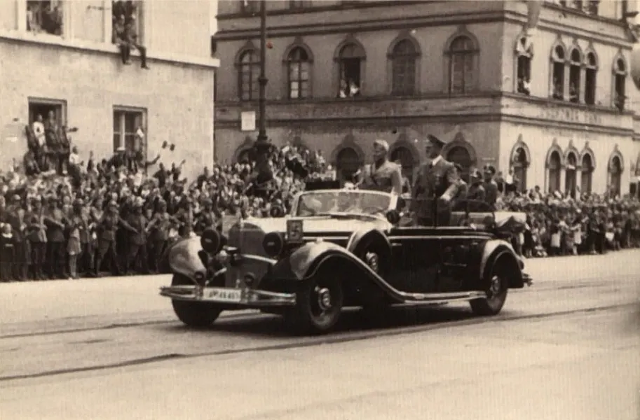 Historical photo of Adolf Hitler in an open car passing crowds giving the Nazi salute in Munich.