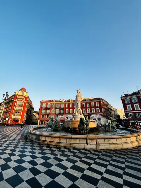Fontaine du Soleil (Sun Fountain) in Nice, with the statue of Apollo and bronze figures, surrounded by red buildings under...