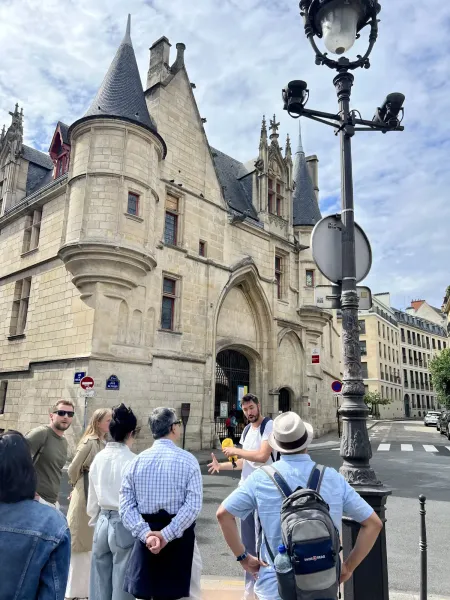 Tour guide addressing a small group of tourists in front of the historic Hôtel de Sens building in Paris on a cloudy day.