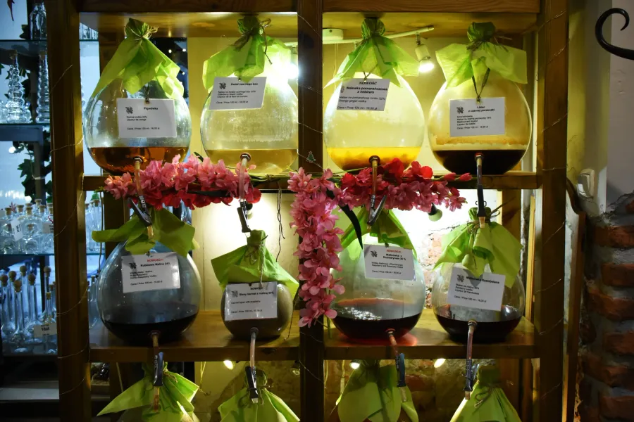 Glass dispensers filled with traditional Polish nalewka liqueurs on wooden shelves in a Krakow shop.