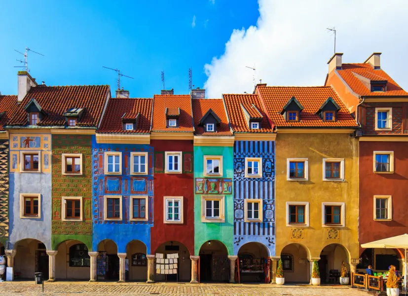 Row of colorful historic houses with tiled roofs and arched ground floors on a cobblestone square in Poznan.