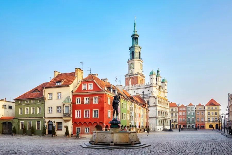 Cobblestone market square with a fountain and Apollo statue, colorful historic buildings, and a large town hall tower unde...