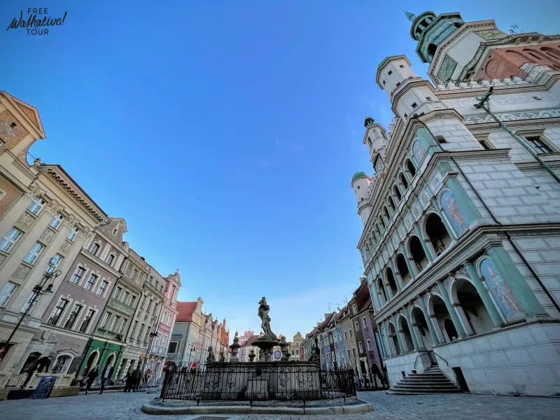 Panoramic view of Poznań Old Market Square with colorful tenement houses, a large fountain, and the ornate Renaissance Tow...