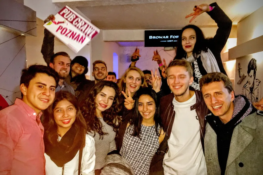 Group of smiling young adults holding a "Pub Crawl Poznan" sign indoors, with a "Browar Fortuna" sign in the background.