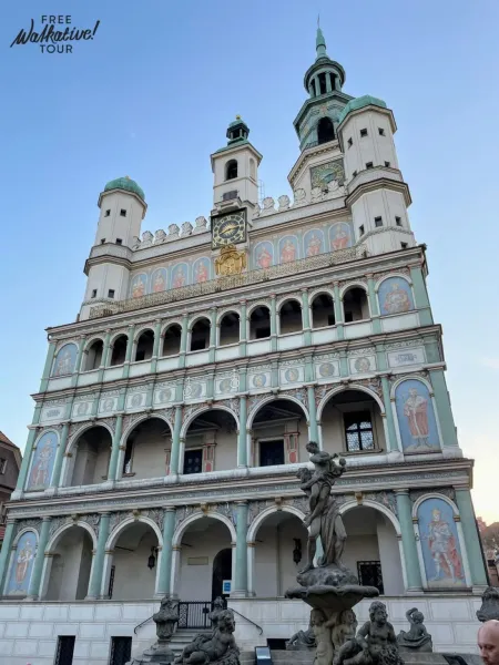 Renaissance Town Hall in Poznan with ornate facade, arcades, frescoes, clocks, and green spires under a blue sky, fountain...