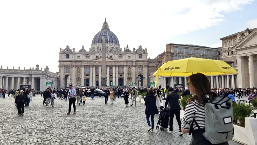 Crowded St. Peter's Square with St. Peter's Basilica, an obelisk, and colonnades under a partly cloudy sky. A yellow Walka...