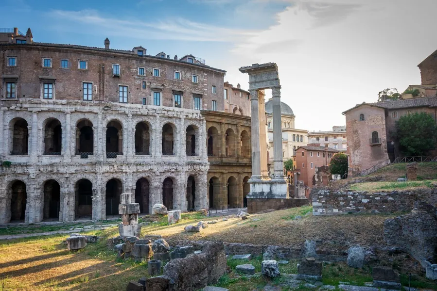 Ancient Theatre of Marcellus ruins with arched facade, modern buildings above, and Roman columns and debris in foreground.