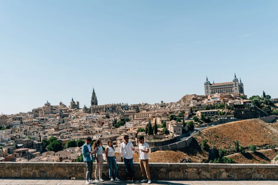 A group of people at a viewpoint overlooking the historic city of Toledo, Spain, on a sunny day.