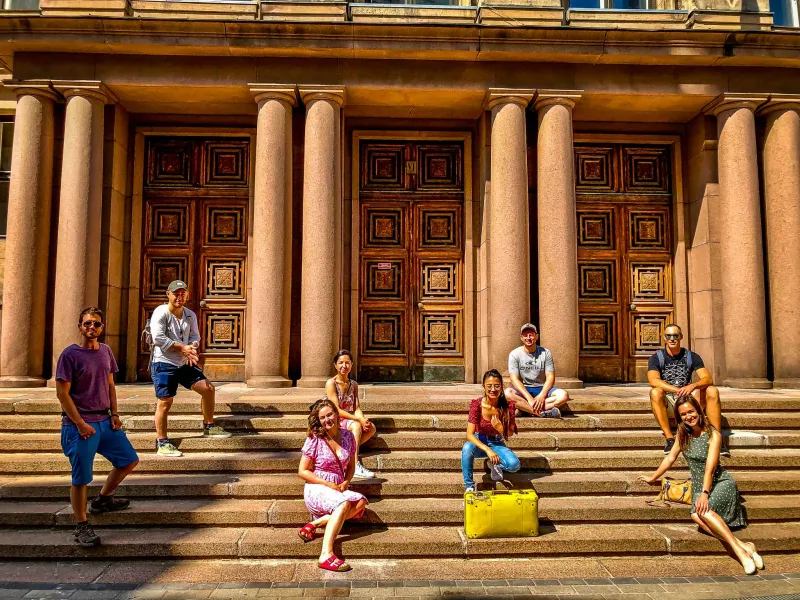 Happy tourists pose on the steps of a beautiful building in Helsinki.