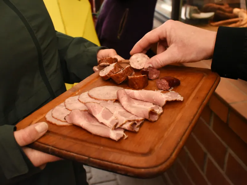 Two people sharing a wooden board with traditional sliced meats and sausage tasting portions.