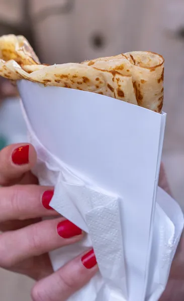 Close-up of a person's hand with red nail polish holding a folded crepe in a white paper holder.