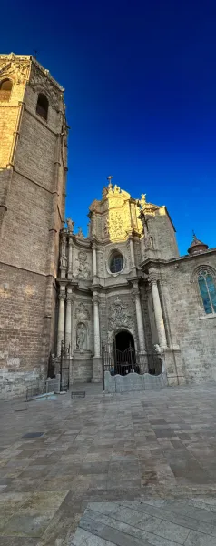 Detailed baroque facade of Valencia Cathedral with a prominent tower and entrance, bathed in sunlight against a deep blue ...