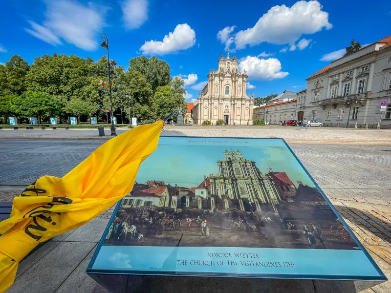 The Church of the Visitandines in Warsaw, a light-colored baroque building, seen behind a historical information board.