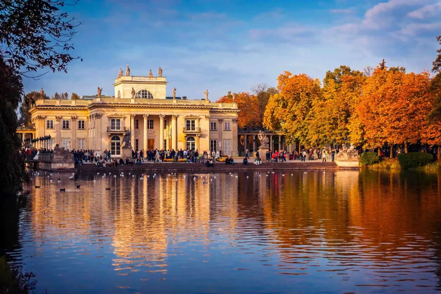 Palace on the Isle at Łazienki Park in Warsaw, reflected in a pond with ducks, surrounded by autumn trees.