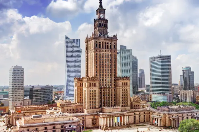 Palace of Culture and Science in Warsaw, a tall building with a clock tower, surrounded by several modern glass skyscraper...