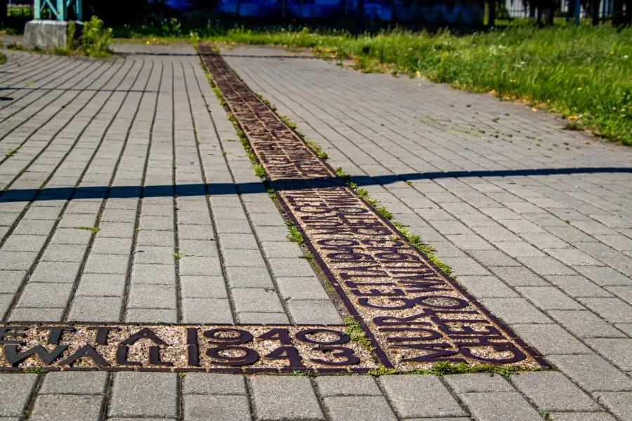 Metal inlay in light gray pavement marking the former Warsaw Ghetto boundary with text 'GETTO WARSZAWSKIE 1940 1943'.