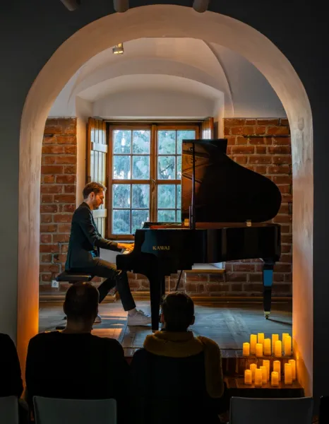 Pianist playing a grand piano during an intimate concert in a brick room with arched doorways in Warsaw.