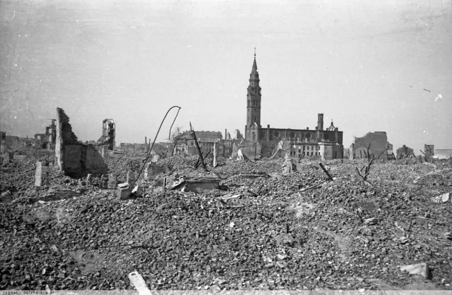 Black and white photo of a city devastated by war, showing a vast field of rubble in the foreground and a damaged church w...