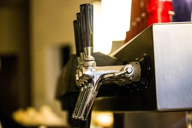 Close-up of three chrome beer taps with black handles on a bar. The background is blurred, showing warm lighting.