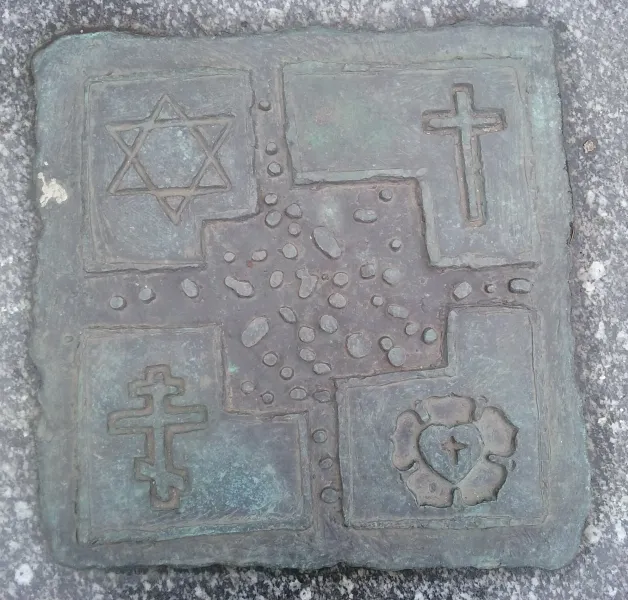 Bronze plaque with four religious symbols: Star of David, Latin cross, Orthodox cross, and Luther rose, embedded in granite.