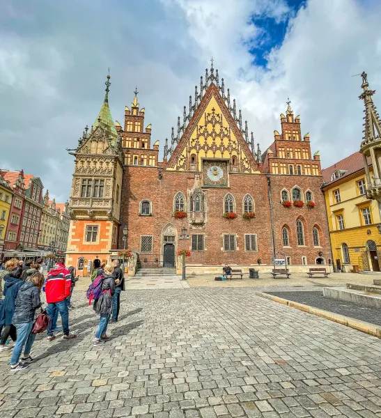 Wroclaw Old Town Hall, a large brick gothic building with a tall clock tower, stands on a cobblestone market square with a...