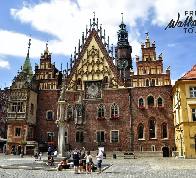 Gothic brick Old Town Hall in Wroclaw with a large clock, ornate gables, and a tall spire. People are gathered in the cobb...