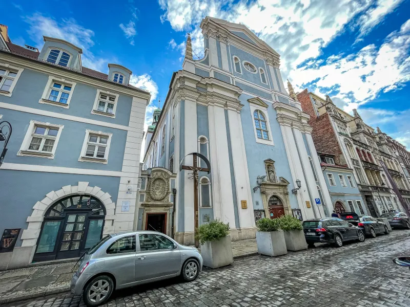 The light blue baroque facade of St. Anthony of Padua Church on a cobblestone street in Wrocław under a blue sky.