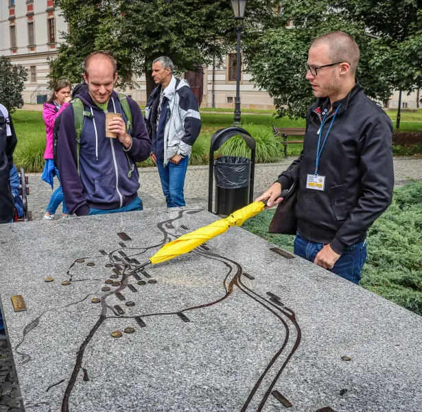Tour guide with a yellow umbrella pointing at a tactile map of Wrocław while a small group of tourists listens.