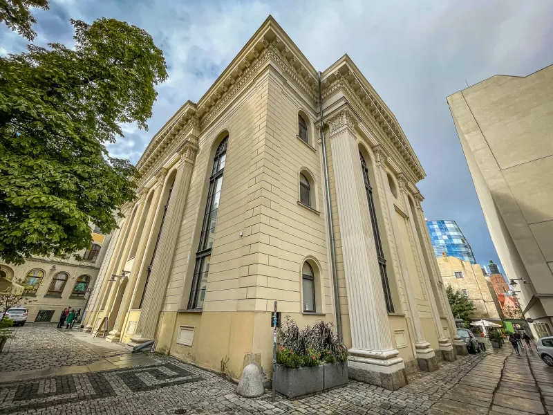 Exterior view of a large, light-yellow classical building with columns and arched windows on a cobblestone street in Wrocław.
