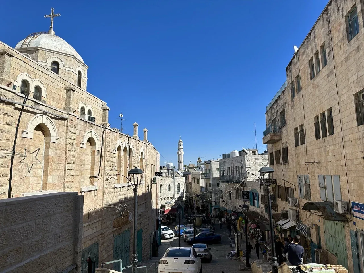 View down a stone street in Bethlehem with a large church building on the left and a distant minaret.