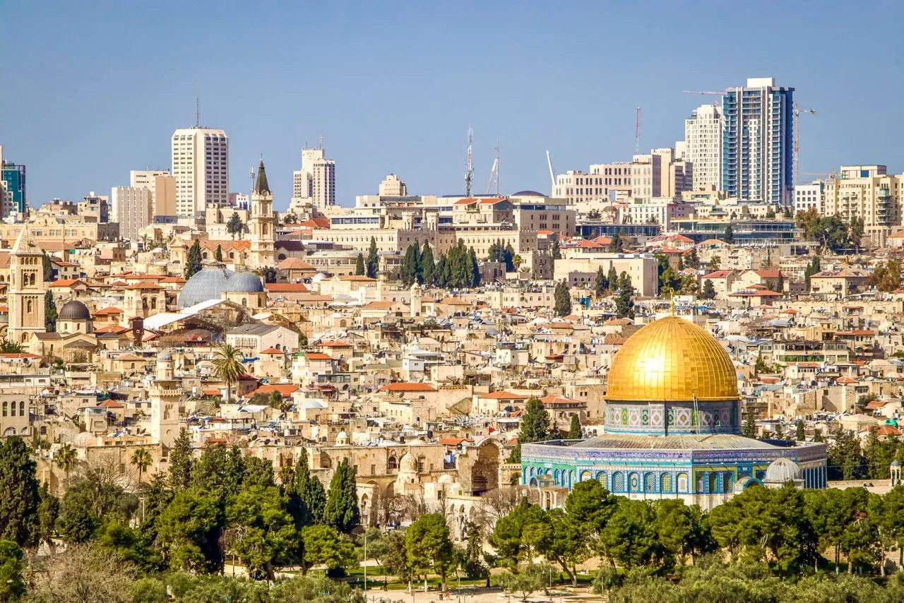View of Jerusalem with the golden Dome of the Rock in the foreground and the Old City buildings and modern high-rises behind.