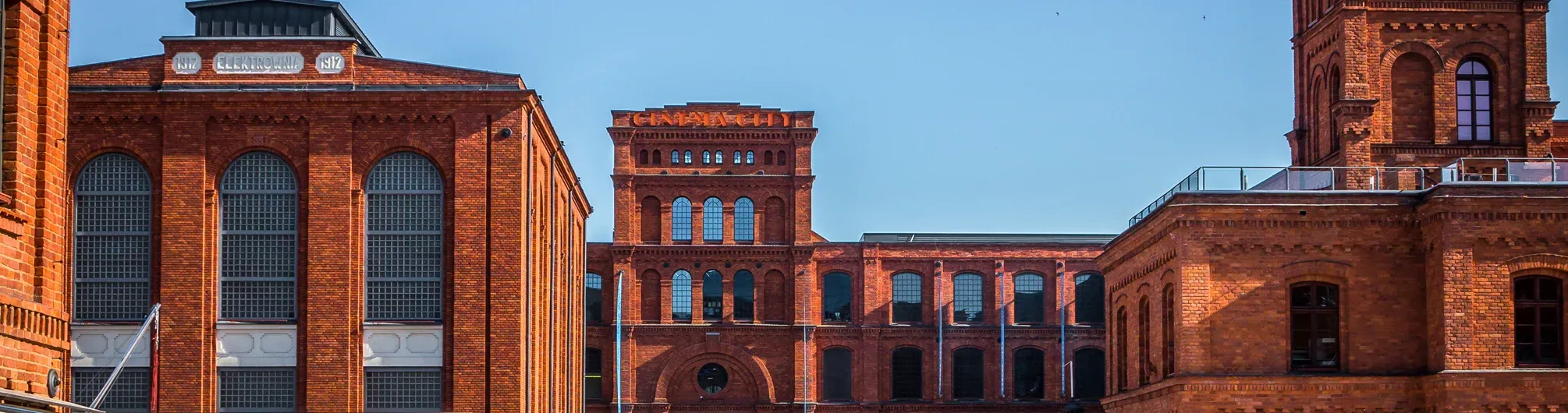Red brick industrial buildings of Manufaktura with arched windows and a clear blue sky.