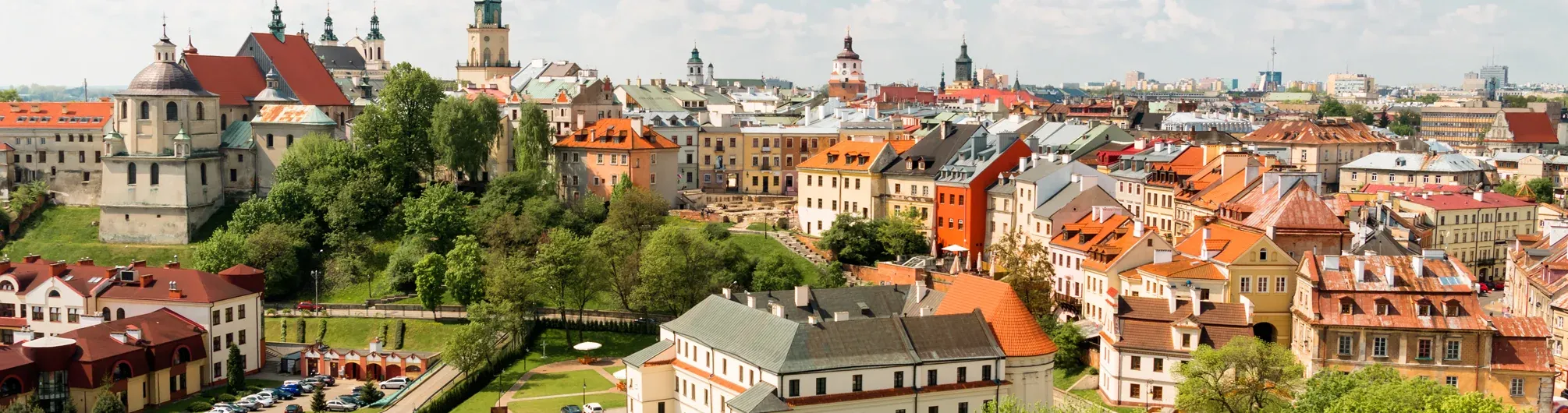 Panoramic view of Lublin Old Town with historic buildings, varied rooftops, green trees, and multiple church spires under a b