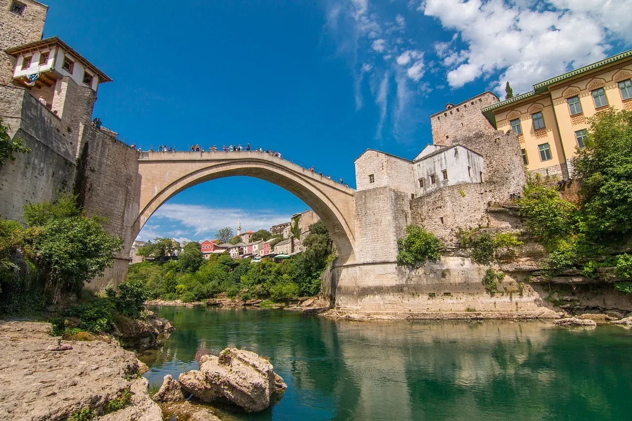 Historic Stari Most bridge in Mostar, Bosnia and Herzegovina, spanning a green river with ancient stone buildings and lush ba