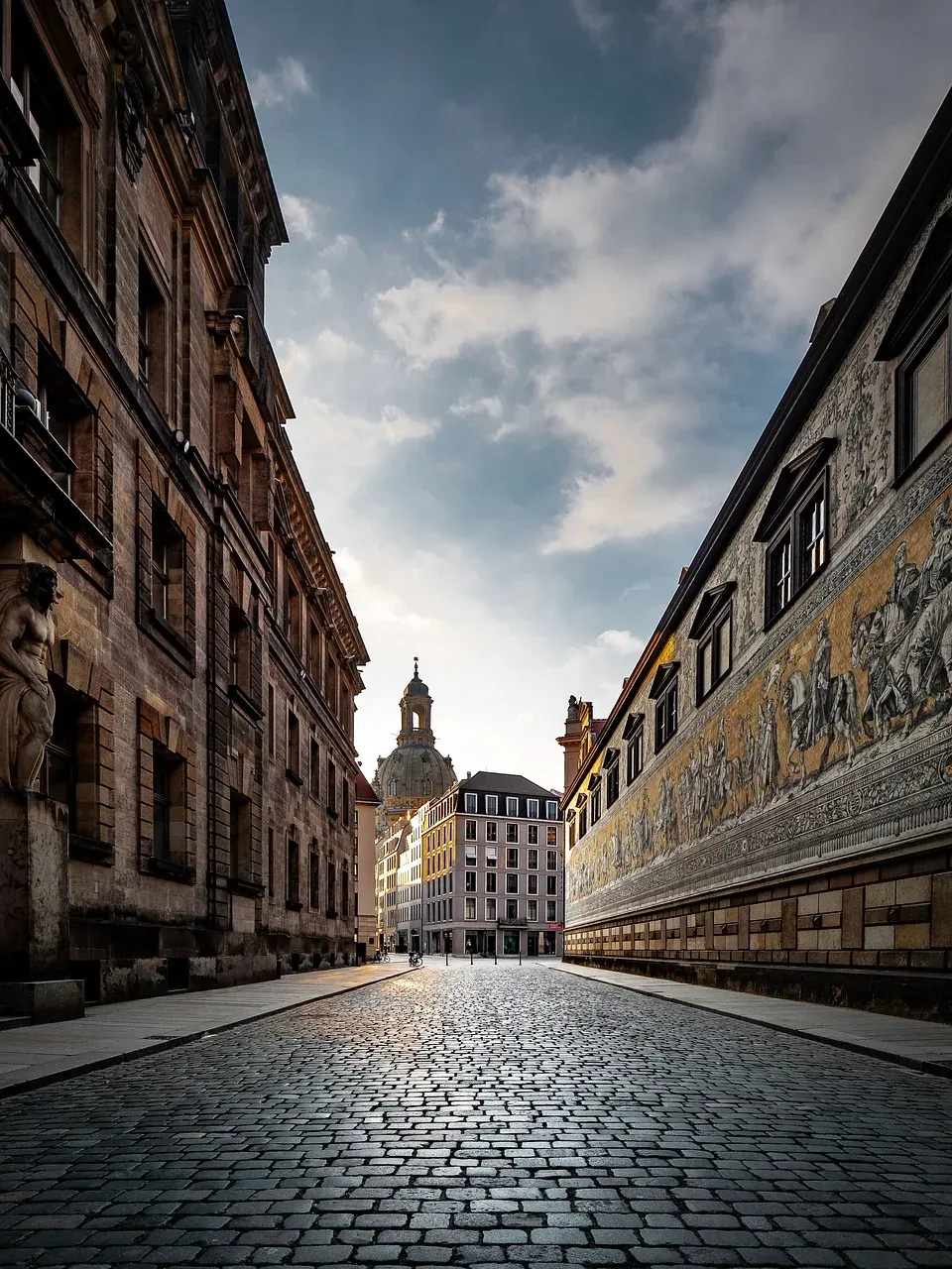 Cobblestone street in Dresden, Germany, with historic buildings and a fresco.