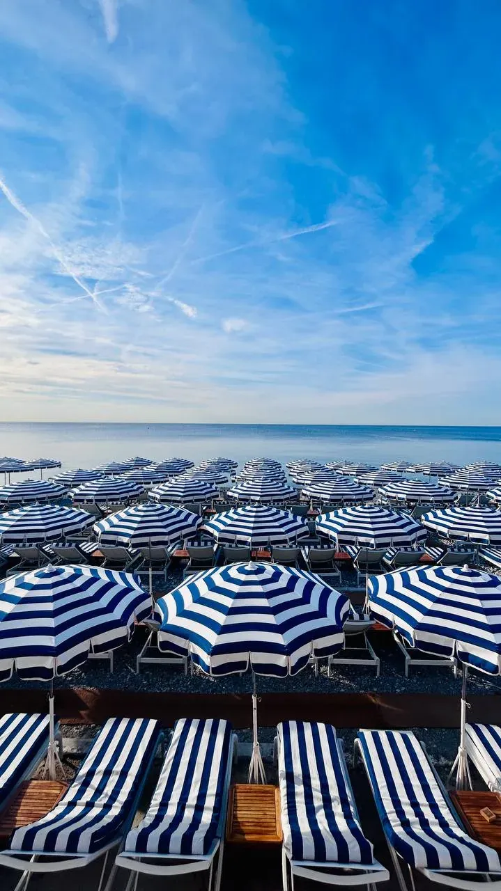 Rows of blue and white striped beach umbrellas and chairs on a Nice beach.