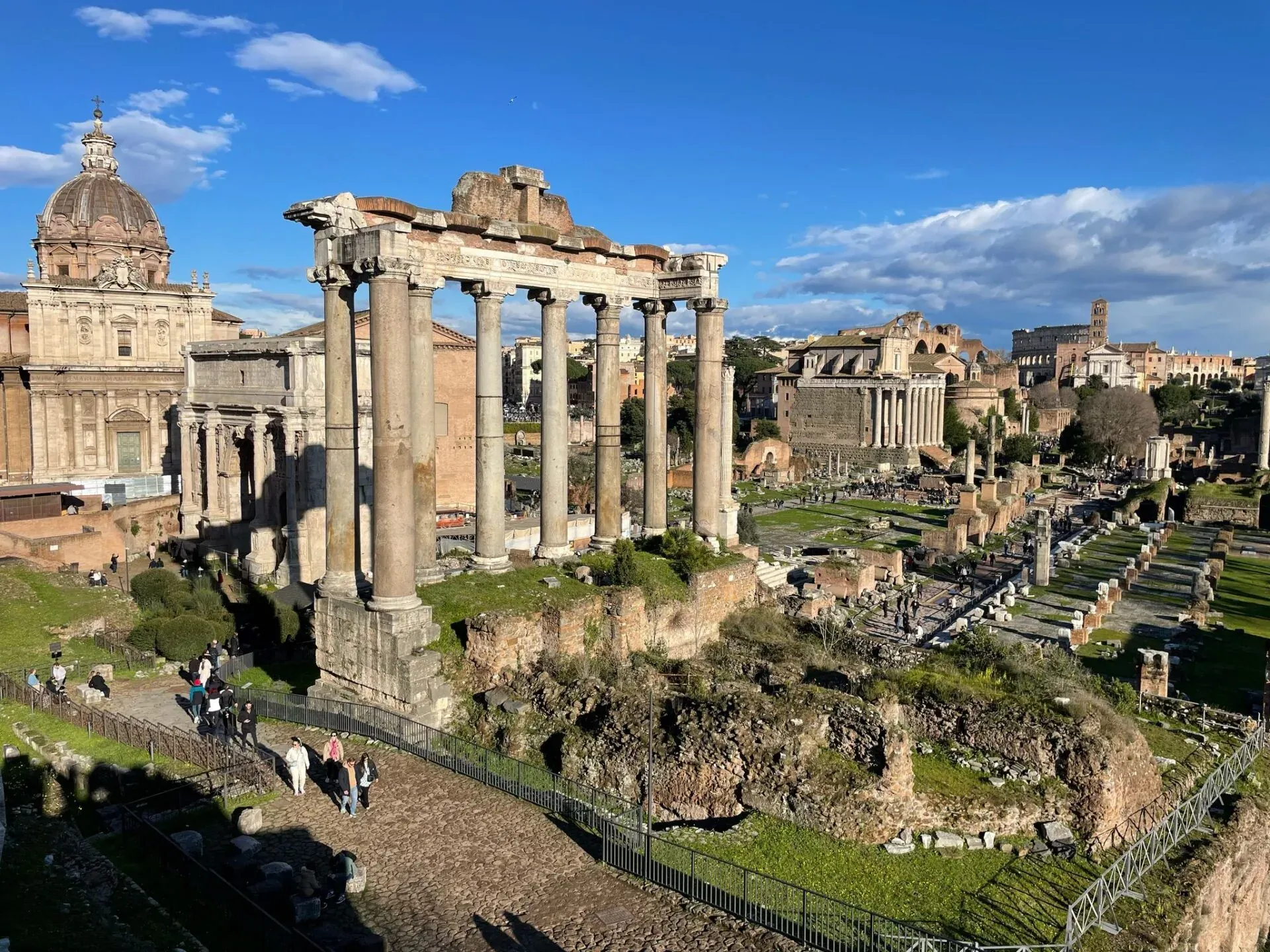 Panoramic view of the Roman Forum in Rome, Italy, with tourists exploring the ancient ruins.