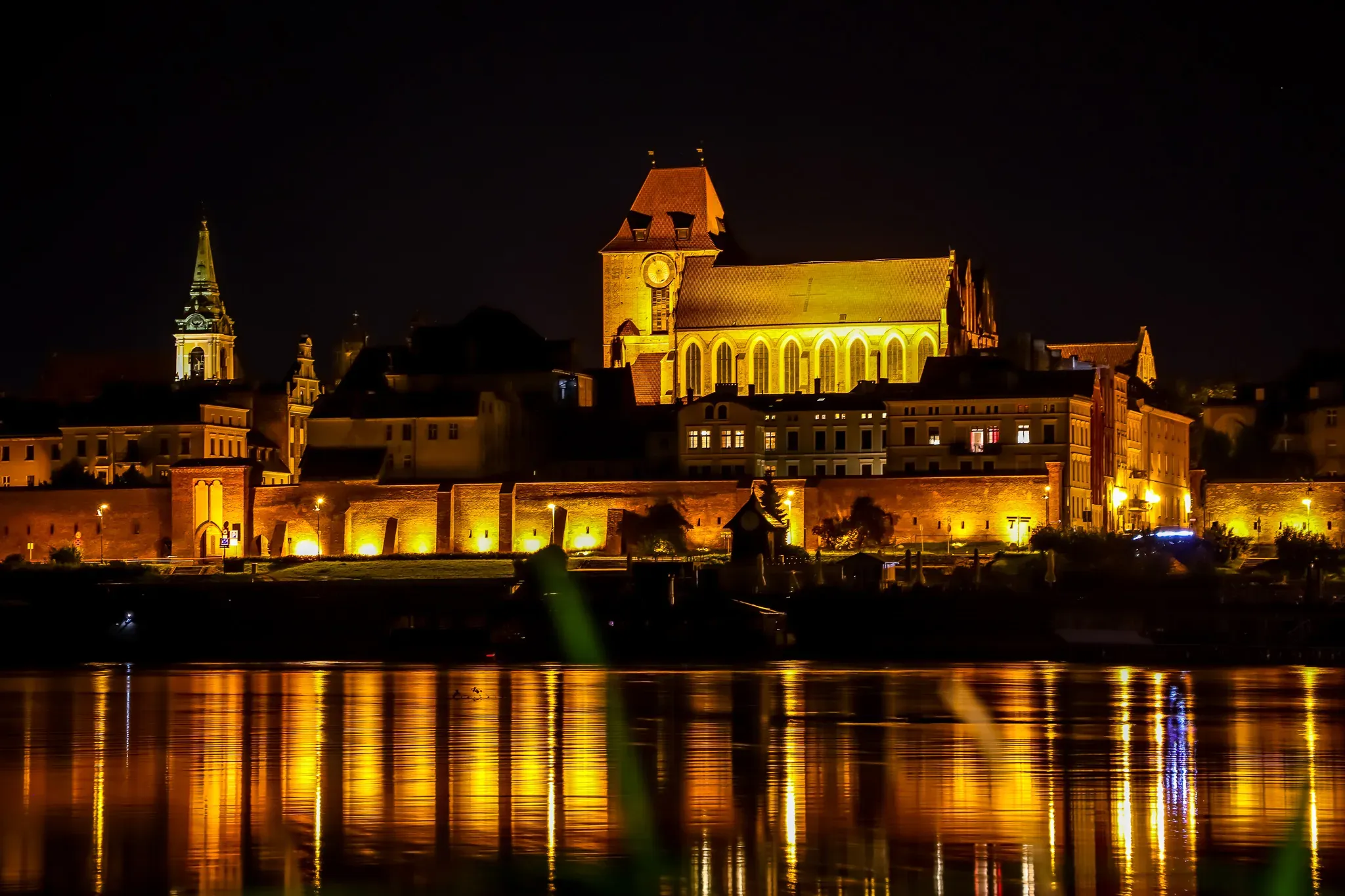 Night view of Toruń's Old Town reflected in the Vistula River.