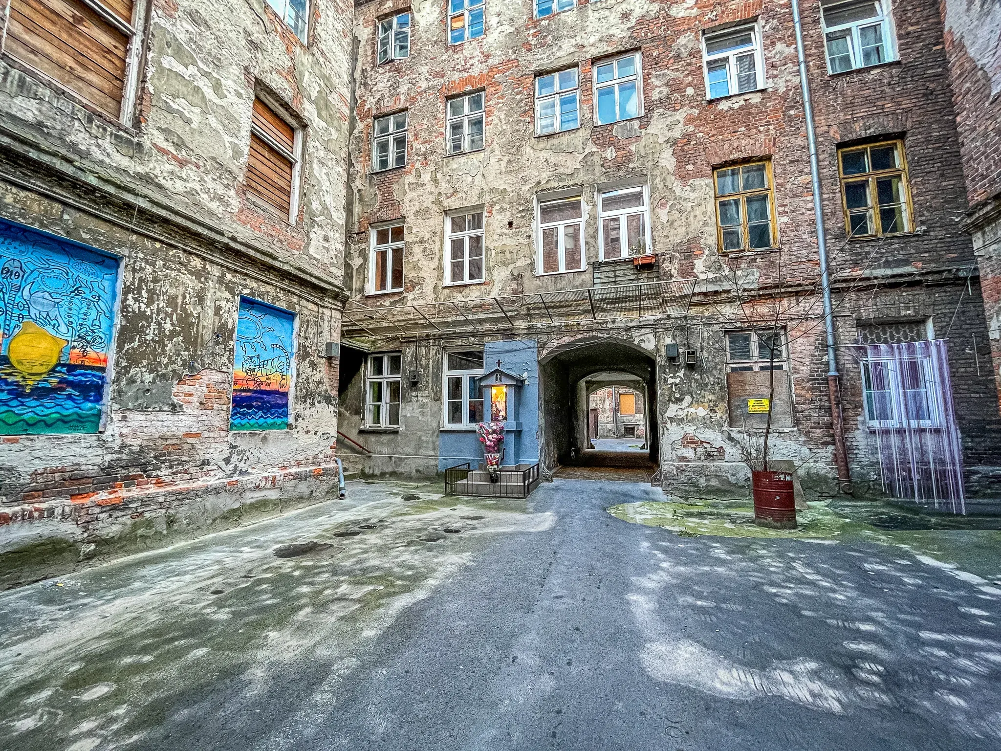 Explore a hidden Warsaw courtyard with aged brick buildings, street art, and a small shrine.