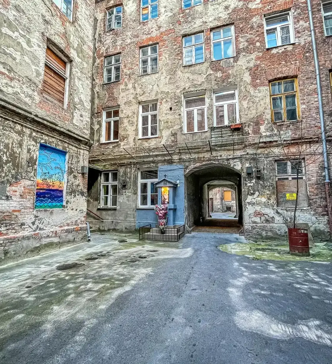 Explore a hidden Warsaw courtyard with aged brick buildings, street art, and a small shrine.